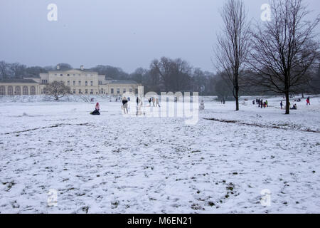 Les adultes et les enfants jouer dans la neige sur Hampstead Heath en face de Kenwood House à Londres après une chute de neige et de froid en hiver 2018. Banque D'Images