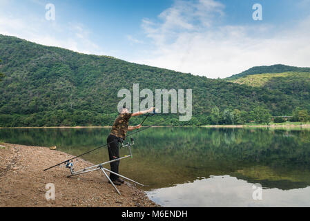 Aventures de pêche, pêche à la carpe. Angler avec t-shirt camouflage et une canne à pêche à la main, est l'appât casting Banque D'Images