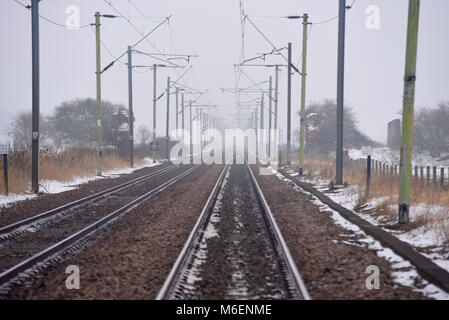 Les voies de chemin de fer sur un jour brumeux à un passage à niveau automatique illustrant le danger de l'absence de visibilité d'un train qui approche. À l'électricité. Portique... Banque D'Images