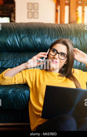 Femme assise sur le sol à l'aide d'un ordinateur portable et téléphone mobile tenant une tasse de café. Banque D'Images