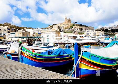 Bateaux de pêche traditionnelle dans le port avec l'église Notre Dame de Lourdes sur la colline à l'arrière, Mgarr, Gozo, Malte, l'Europe. Banque D'Images