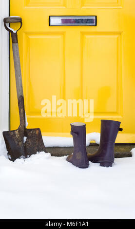 Bottes Wellington et la pelle à l'extérieur d'une porte avant dans la neige. Banque D'Images