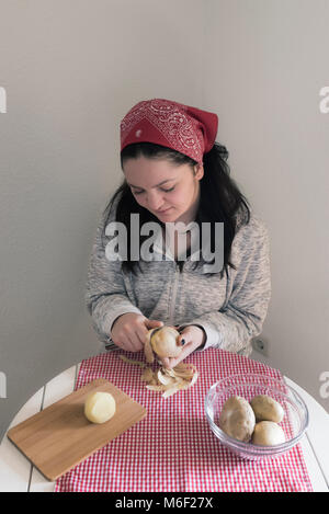 Jeune femme, habillé décontracté, préparer un repas avec des pommes de terre, dans sa cuisine sur un tableau blanc. Banque D'Images