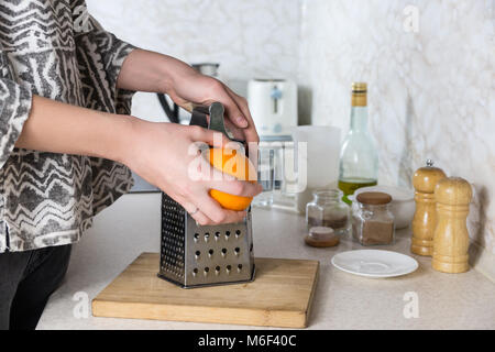 Râper le zeste d'orange. Râpe à utiliser les mains des femmes à faire peler en environnement de cuisine Banque D'Images