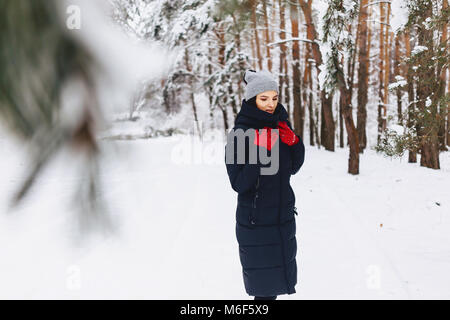 La jeune fille marche dans une forêt couverte de neige parmi les pins en rouge et des gants pose tourne Banque D'Images