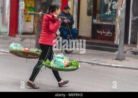 Une femme porte des légumes dans les paniers suspendus à partir de son pôle comptable de bambou à Hanoi, Vietnam Banque D'Images