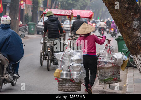 Une femme porte des casseroles en aluminium à vendre dans des paniers suspendus à partir de son pôle comptable de bambou à Hanoi, Vietnam Banque D'Images