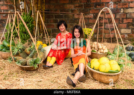 Deux femmes s'asseoir entre les poteaux de bambou portant des paniers et rempli de fruits à Hanoi, Vietnam alors qu'ils célèbrent le Nouvel An chinois. Banque D'Images