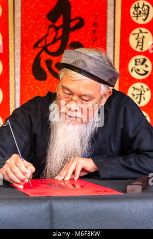 Un vieil homme vietnamien avec une longue barbe blanche utilise un pinceau pour dessiner des caractères chinois calligraphie à Hanoi, Vietnam Banque D'Images