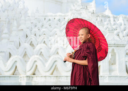 MANDALAY, MYANMAR, -le 11 décembre 2017 asiatique non identifié : jeune moine tenant un parapluie rouge sur la Mya Thein Tan Mingun pagode à Mandalay, Myanmar. Banque D'Images