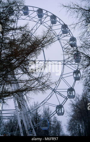 Fragment d'une grande roue, visible à travers les branches des arbres d'hiver dans un sombre brouillard météo Banque D'Images