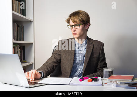 Beau jeune personne dans la lecture lunettes au milieu moderne et épuré. Jeune homme étudiant travaille avec des livres et un ordinateur portable sur accueil cession ou pro Banque D'Images