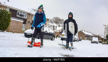 Deux garçons à pied sur une rue couverte de neige tirant des traîneaux et des body boards pour aller jouer dans la neige de mars et profitez au maximum de fermeture de l'école. Banque D'Images