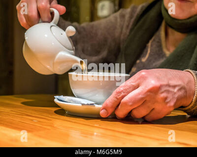 Vue rapprochée tea pot verre coulée en tasse dans la haute main. Banque D'Images