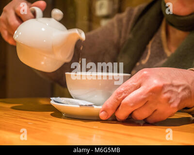 Vue rapprochée tea pot verre coulée en tasse dans la haute main. Banque D'Images