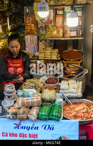 Une femme regarde son smartphone lors de l'attente pour les clients de son street food sur un sentier à Hanoi, Vietnam Banque D'Images