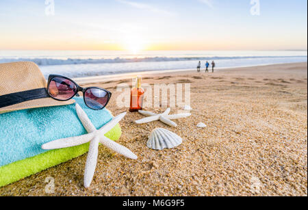 Accessoires d'été comme les lunettes, serviettes, chapeau, crème solaire, de coquillages et d'étoiles de mer sur la plage de sable au Portugal Banque D'Images