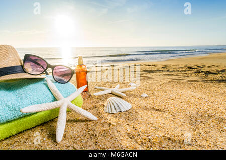 Accessoires d'été comme les lunettes, serviettes, chapeau, crème solaire, de coquillages et d'étoiles de mer sur la plage de sable au Portugal Banque D'Images