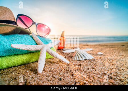 Accessoires d'été comme les lunettes, serviettes, chapeau, crème solaire, de coquillages et d'étoiles de mer sur la plage de sable au Portugal Banque D'Images