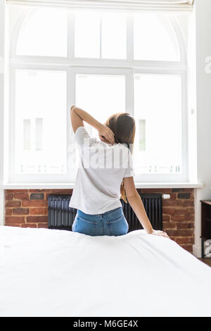 Jeune femme assise au lit s'étend après le réveil le matin. Dame souffrant de Mal de dos après le sommeil, ressent de l'inconfort en raison de mauvais matelas, o Banque D'Images