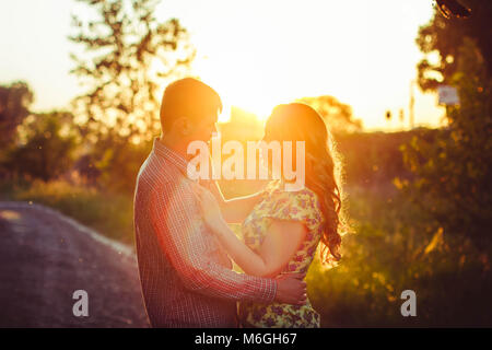 Un couple aimant se regarder dans les derniers rayons du soleil, dans un champ près de la route. Banque D'Images