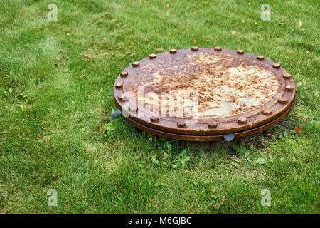 Revêtement métallique rouillé rond de trou d'homme dépassé sur le système d'évacuation de la pluie situé sur la pelouse avec une herbe verte luxuriante Banque D'Images