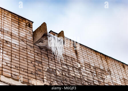 Les glaçons gelés pendent d'une auge en béton sur un vieux mur de briques, vestiges du froid de l'hiver Banque D'Images