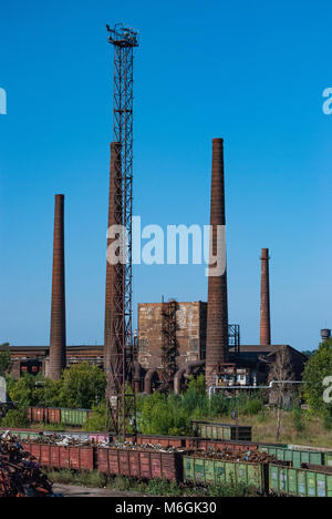 Complexe industriel abandonné, avec de grandes cheminées altérées surplombant les bâtiments délabrés contre un ciel bleu clair Banque D'Images