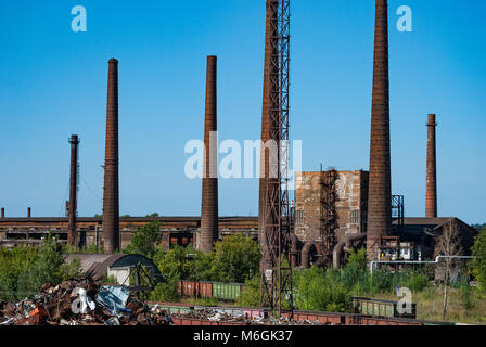 Complexe industriel abandonné, avec de grandes cheminées altérées surplombant les bâtiments délabrés contre un ciel bleu clair Banque D'Images