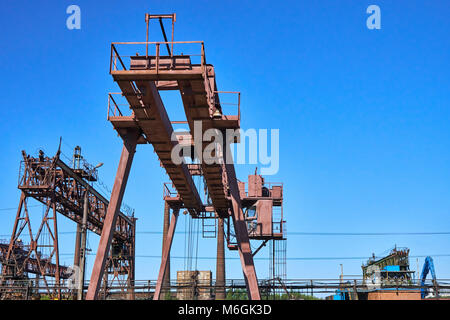 Grue à portique métallique surplombant une déchirure pleine de débris métalliques, avec un ciel bleu clair en arrière-plan Banque D'Images