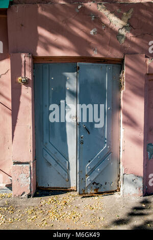 Vieilles portes en métal double avec peinture bleue sur une façade de bâtiment fissurée rose usée Banque D'Images