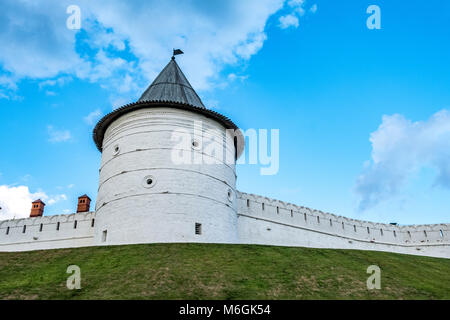 Majestueuse tour de forteresse médiévale blanche avec un toit conique au sommet d'une colline herbeuse, symbolisant la protection historique sous un vaste ciel bleu avec des nuages Banque D'Images