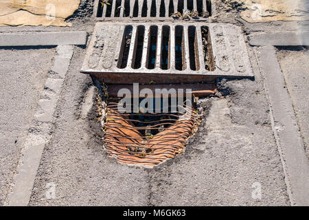 Drain pluvial intégré dans l'asphalte fissuré, montrant des signes de dégâts d'eau et d'usure Banque D'Images