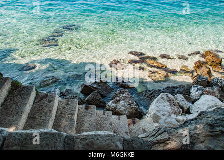 Vue sereine sur les marches en pierre grossière descendant dans l'eau bleue fascinante de l'océan. De grands rochers bordent les marches et sont répartis sur le fond de la mer Banque D'Images