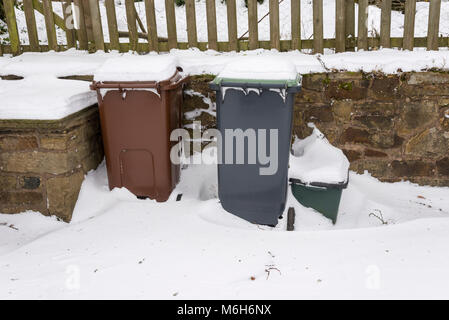 Wheelie bins couverts dans la neige profonde à côté d'un mur de pierre. Banque D'Images