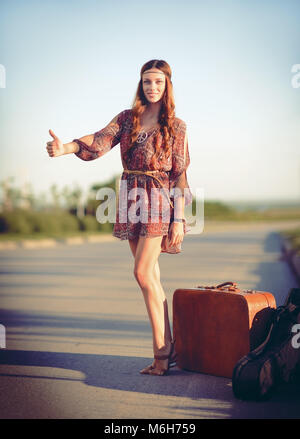 Jolie jeune femme hippie de l'auto-stop sur la route, à l'heure du coucher de soleil. Banque D'Images