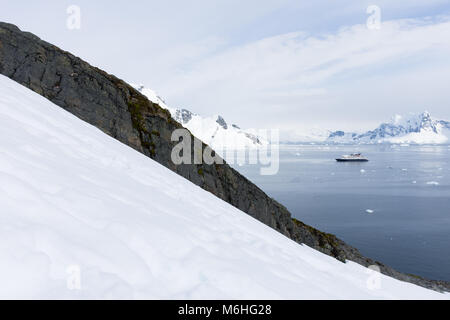 Un navire ancré dans le Paradise Bay, l'Antarctique avec la neige et une crête de rocher dans l'avant-plan et la baie, d'expédier et de montagnes couvertes de neige dans la zone Banque D'Images
