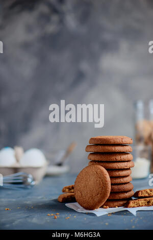 Oatmeal Cookies dans une pile soignée sur un arrière-plan en pierre avec des ingrédients hors focus. Concept de cuisson en high key avec copie espace. Banque D'Images