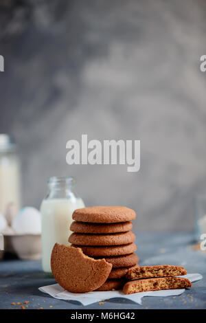Oatmeal Cookies dans une pile soignée sur un arrière-plan en pierre avec des ingrédients hors focus. Concept de cuisson en high key avec copie espace. Banque D'Images