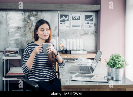 Asian businesswoman prendre une pause-café après avoir travaillé avec visage souriant, heureux de la vie de bureau concept,femme qui travaille au bureau d'accueil moderne. Banque D'Images