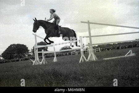 1940, historiques, une jeune fille à cheval -sans casque, cap ou quoi que ce soit sur la tête - montrant une bonne technique sautant par-dessus un obstacle ou une clôture à un saut d'extérieur, England, UK. Banque D'Images