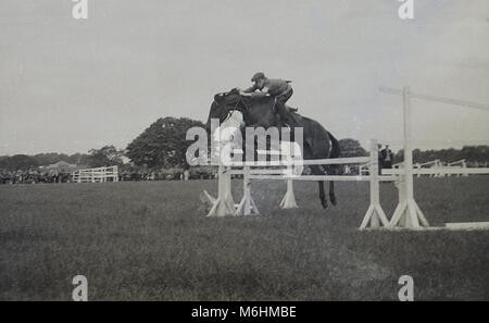 1940, historique, un jeune garçon un Cheval sautant par-dessus un obstacle ou une clôture à un saut d'extérieur, England, UK. Sur sa tête est un cap pas un casque. Banque D'Images