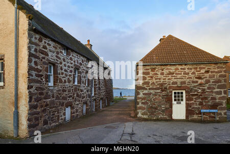 Maisons et bâtiments de pêche à Stonehaven, un village de pêcheurs sur la côte Est de l'Ecosse. Un homme marche le long du sentier du littoral à l'arrière-plan. Banque D'Images