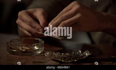 Young mans mains rouler cigarette de la marijuana médicale pour soulager la douleur chronique Banque D'Images