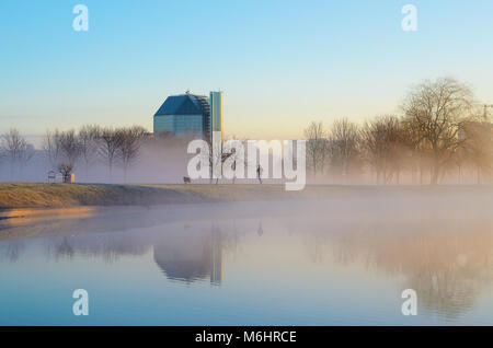 Biélorussie, Minsk - 4 Avril 2017 : Une jeune femme jogging avec un chien le long du fleuve dans les écrivains Park, près de la Bibliothèque nationale au début des temps brumeux Banque D'Images