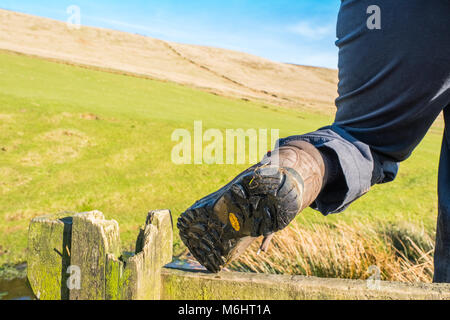 Walker femelle avec bottes de randonnée escalade sur un montant sur un sentier de Peak District Banque D'Images