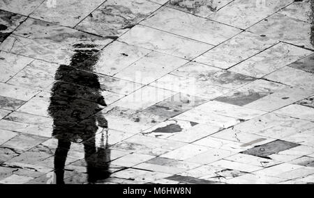 Blurry femme transportant un sac d'épicerie d'ossature réflexion sur trottoir à motifs des pluies en noir et blanc Banque D'Images