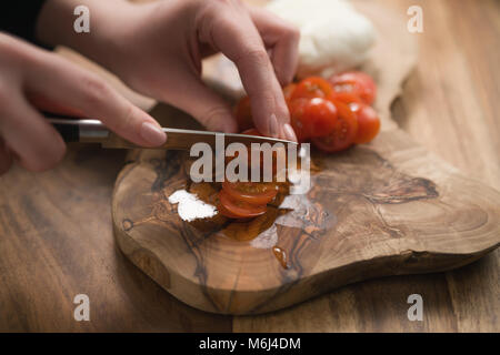 La main de l'adolescence féminine de trancher les tomates cerise avec un couteau sur planche de bois Banque D'Images