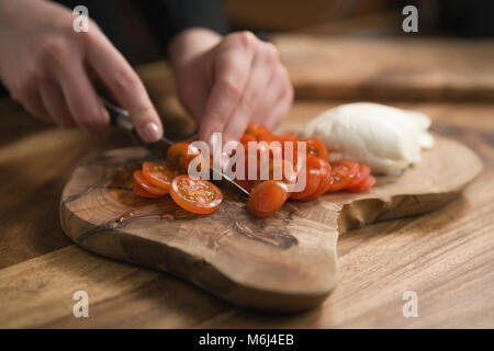 La main de l'adolescence féminine de trancher les tomates cerise avec un couteau sur planche de bois Banque D'Images