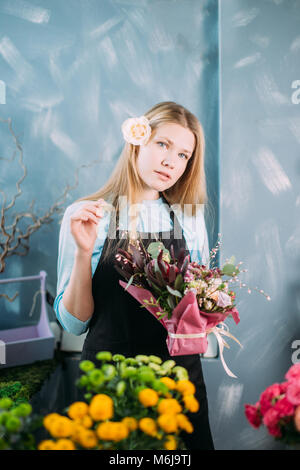 Belle fille blonde debout devant la table avec fleur et looking at camera Banque D'Images